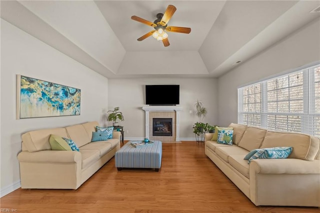 living room with light wood-type flooring, a raised ceiling, a ceiling fan, baseboards, and a tile fireplace