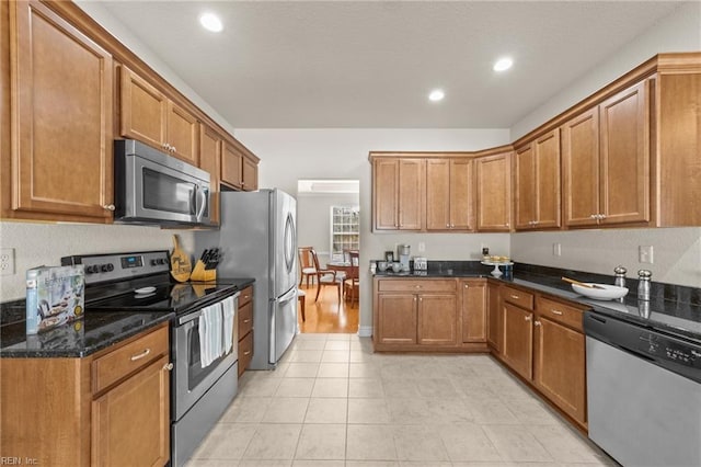 kitchen featuring dark stone counters, light tile patterned floors, recessed lighting, brown cabinets, and appliances with stainless steel finishes