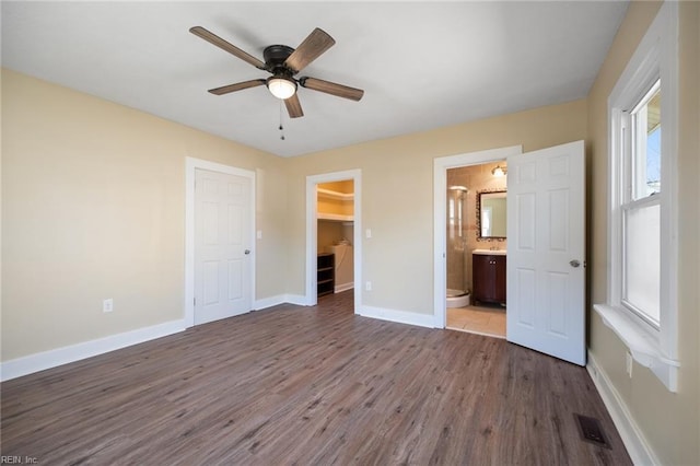 unfurnished bedroom with wood finished floors, baseboards, ensuite bath, a closet, and a walk in closet