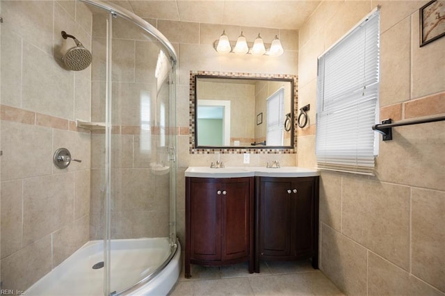 bathroom with tile patterned flooring, double vanity, a stall shower, tile walls, and a sink