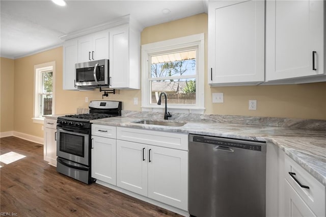 kitchen with dark wood-type flooring, a sink, white cabinetry, appliances with stainless steel finishes, and light stone countertops