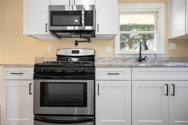 kitchen with a sink, stainless steel appliances, light stone countertops, and white cabinets