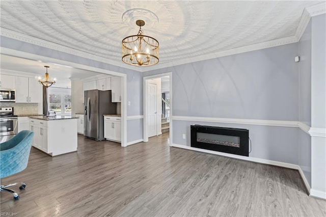 unfurnished living room featuring a fireplace, ornamental molding, wood finished floors, and a chandelier