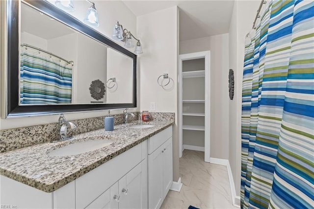 full bath with a sink, baseboards, marble finish floor, and double vanity