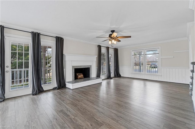 unfurnished living room with a wainscoted wall, wood finished floors, a ceiling fan, and ornamental molding