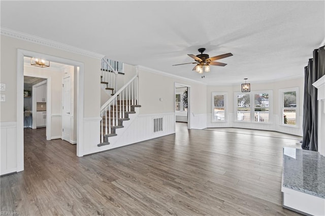 unfurnished living room featuring ornamental molding, wood finished floors, stairs, and ceiling fan with notable chandelier