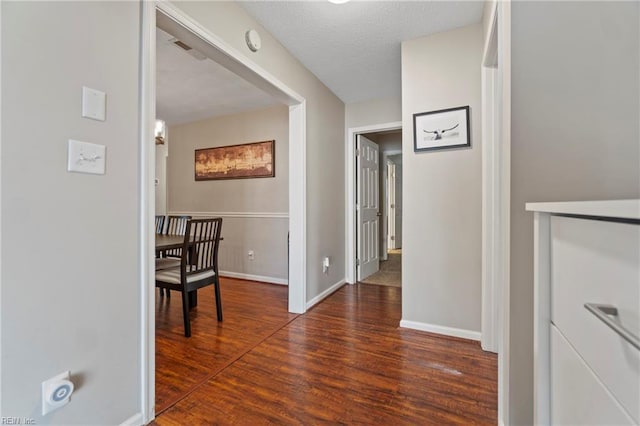 hallway with visible vents, baseboards, a textured ceiling, and wood finished floors