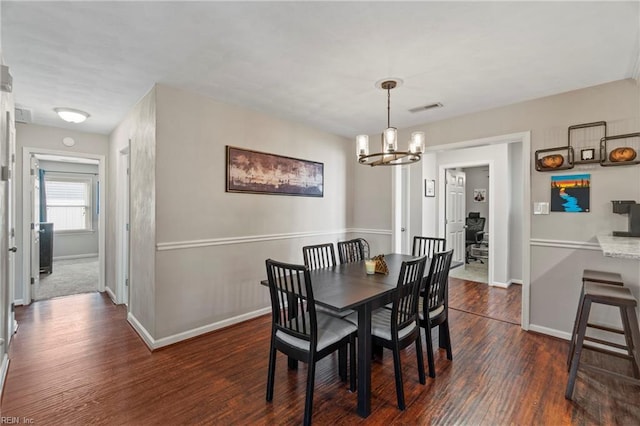 dining space featuring dark wood finished floors, visible vents, a chandelier, and baseboards