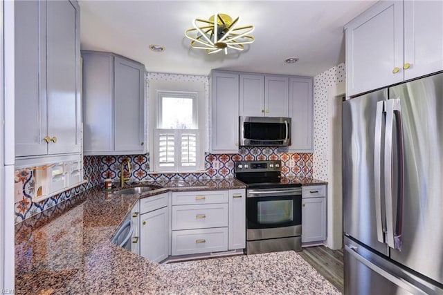 kitchen featuring backsplash, dark stone countertops, stainless steel appliances, and a sink