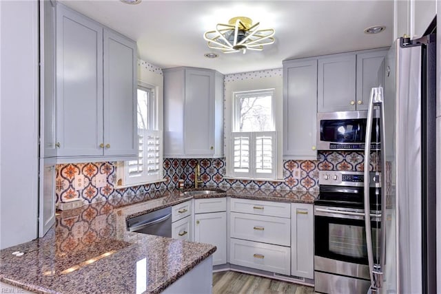 kitchen with dark stone counters, a peninsula, a sink, stainless steel appliances, and backsplash