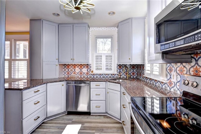 kitchen featuring a sink, dark stone countertops, backsplash, stainless steel appliances, and light wood-style floors