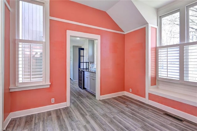 spare room with visible vents, lofted ceiling, beverage cooler, wood finished floors, and baseboards