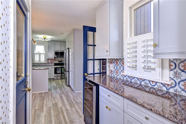 kitchen featuring dark stone countertops, backsplash, stainless steel appliances, wine cooler, and light wood-style floors