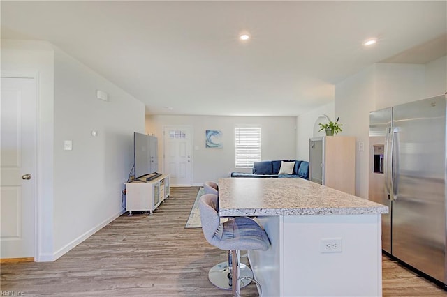 kitchen with a breakfast bar, light wood-style flooring, a center island, stainless steel fridge, and light countertops