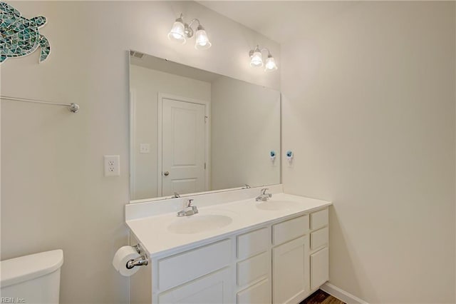 bathroom featuring double vanity, toilet, baseboards, and a sink