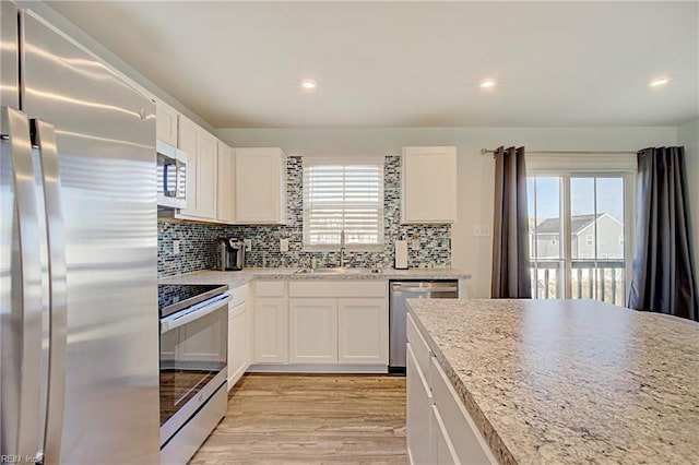 kitchen featuring light wood-style flooring, a sink, stainless steel appliances, white cabinets, and decorative backsplash