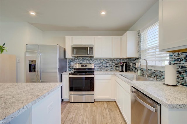 kitchen with backsplash, appliances with stainless steel finishes, light wood-style floors, white cabinets, and a sink