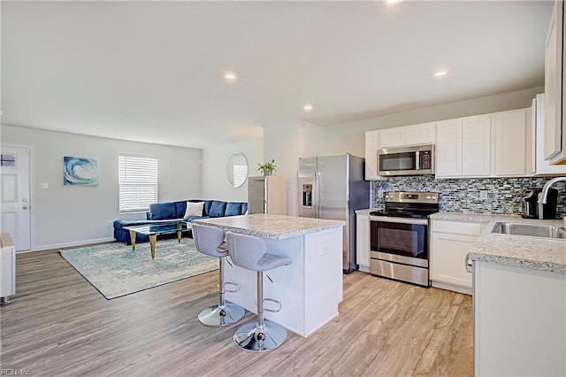 kitchen featuring decorative backsplash, open floor plan, appliances with stainless steel finishes, and a sink