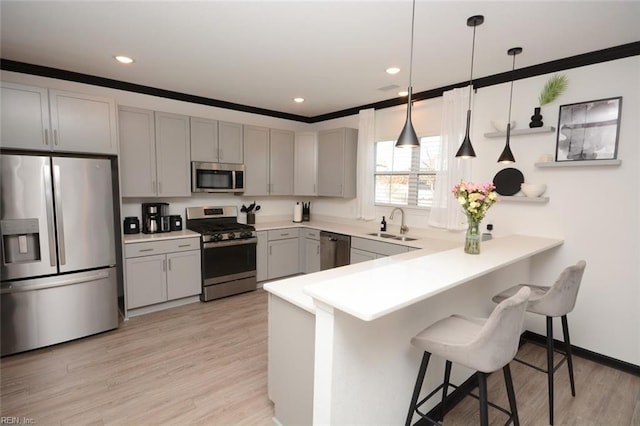 kitchen with a breakfast bar area, a peninsula, gray cabinets, a sink, and stainless steel appliances