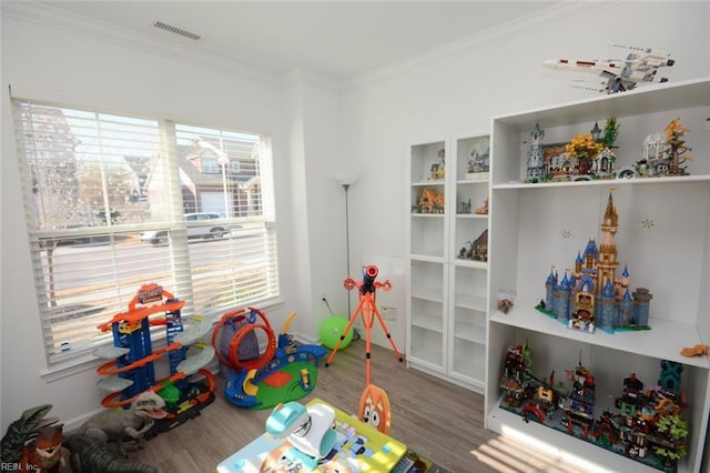 recreation room with visible vents, wood finished floors, and ornamental molding