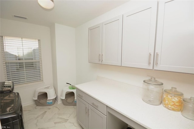 clothes washing area with cabinet space, visible vents, and marble finish floor