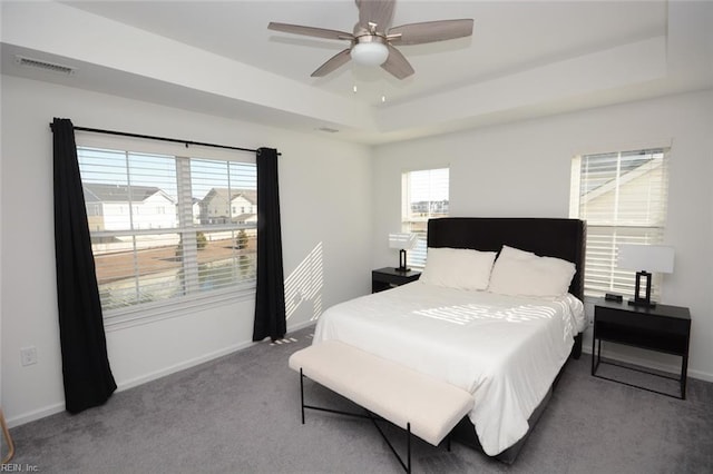 carpeted bedroom with a tray ceiling, visible vents, baseboards, and ceiling fan