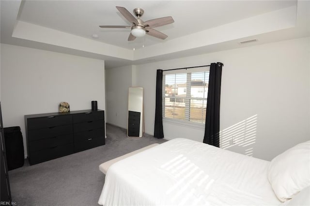 carpeted bedroom with a tray ceiling, visible vents, and ceiling fan