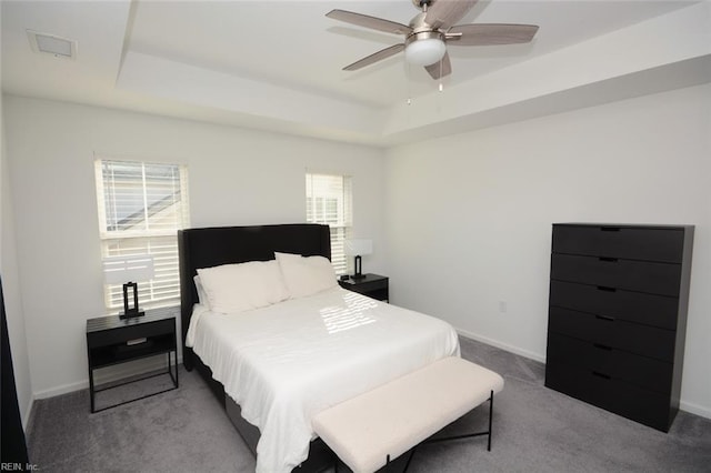 carpeted bedroom with visible vents, multiple windows, baseboards, and a tray ceiling