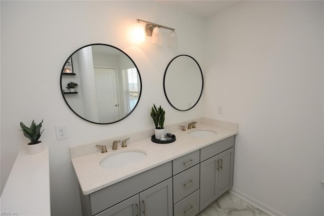 bathroom featuring double vanity, marble finish floor, baseboards, and a sink