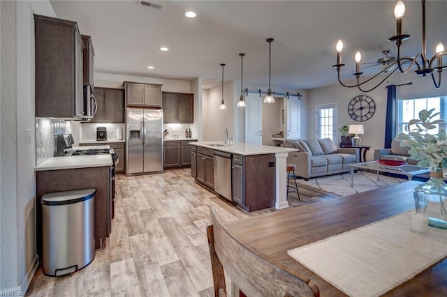 kitchen with dark brown cabinets, open floor plan, a barn door, stainless steel appliances, and a sink