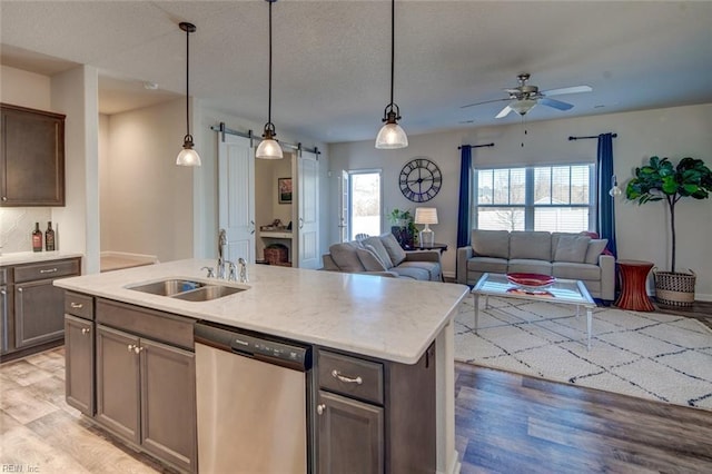 kitchen featuring a sink, open floor plan, a barn door, light wood-style floors, and dishwasher