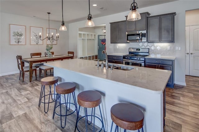 kitchen featuring a kitchen bar, a sink, appliances with stainless steel finishes, light wood finished floors, and decorative backsplash