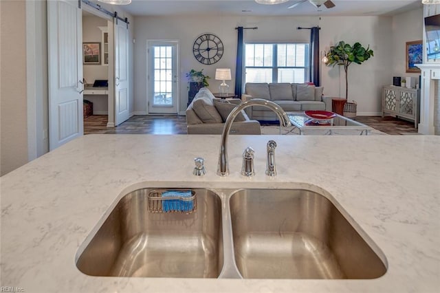 kitchen featuring light stone countertops, ceiling fan, a sink, a barn door, and open floor plan