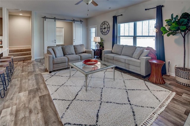 living area with ceiling fan, a barn door, baseboards, and wood finished floors