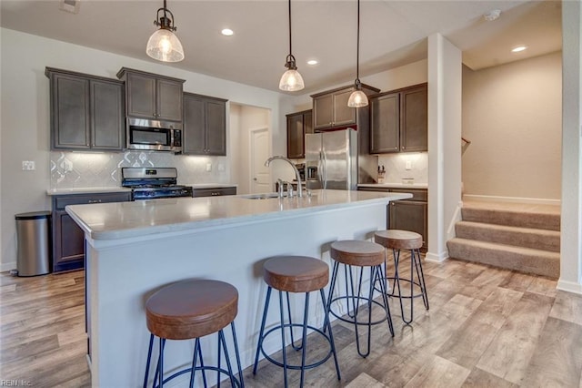 kitchen with a sink, stainless steel appliances, light wood-style floors, and a center island with sink