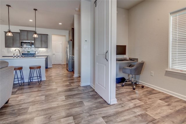 kitchen featuring a breakfast bar area, baseboards, light wood-type flooring, stainless steel appliances, and tasteful backsplash