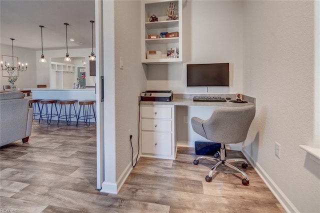 office area featuring an inviting chandelier, built in shelves, wood finished floors, and baseboards