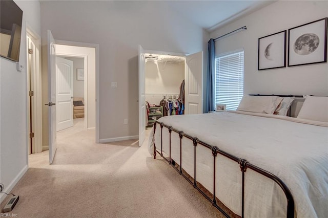 bedroom with a walk in closet, a closet, baseboards, light colored carpet, and vaulted ceiling