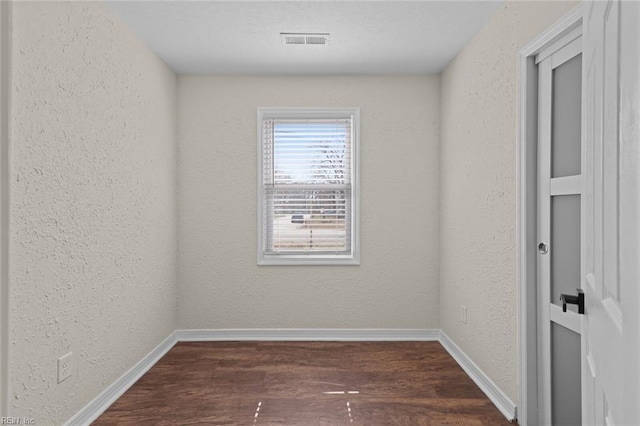 spare room with visible vents, baseboards, dark wood finished floors, and a textured wall