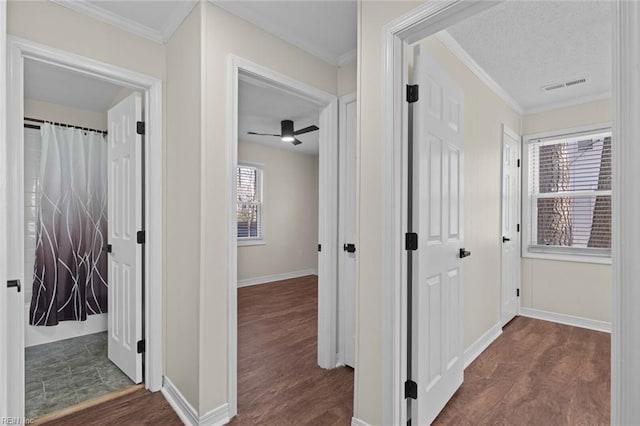 hall featuring visible vents, a textured ceiling, wood finished floors, crown molding, and baseboards