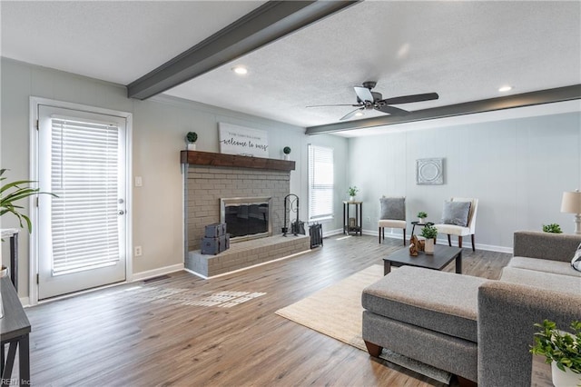 living room with beamed ceiling, a ceiling fan, a textured ceiling, wood finished floors, and a fireplace