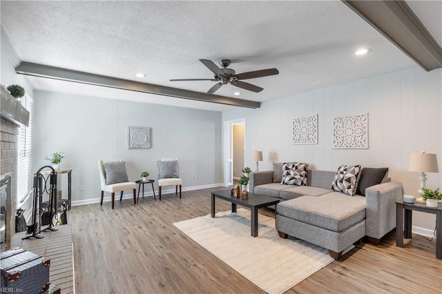 living room featuring beamed ceiling, light wood-style floors, a fireplace, and a textured ceiling