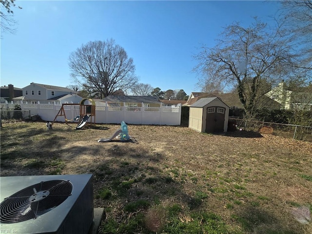 view of yard featuring a storage unit, an outbuilding, a fenced backyard, a playground, and central AC unit