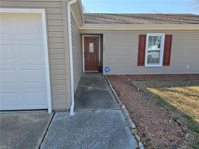 entrance to property featuring a garage and roof with shingles