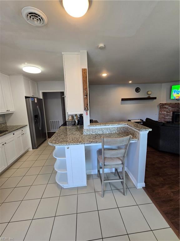 kitchen featuring visible vents, a peninsula, stainless steel refrigerator with ice dispenser, and white cabinetry