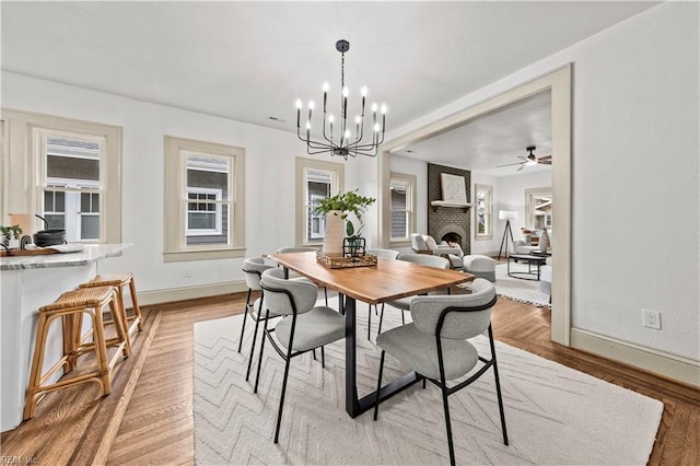 dining room featuring a fireplace, baseboards, light wood finished floors, and a chandelier