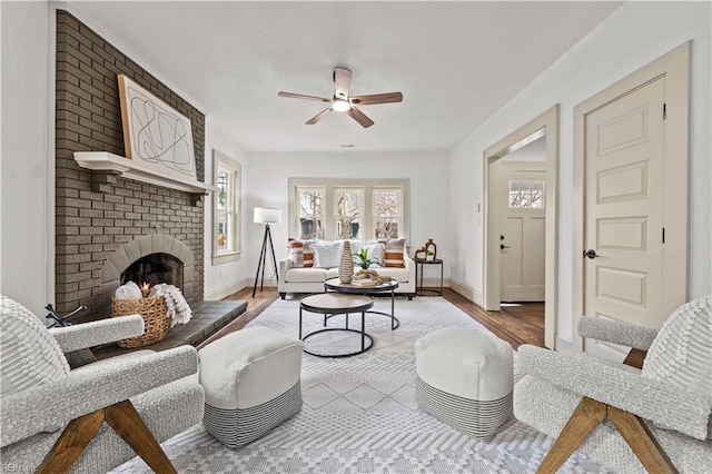 living area featuring a fireplace, baseboards, a ceiling fan, and wood finished floors