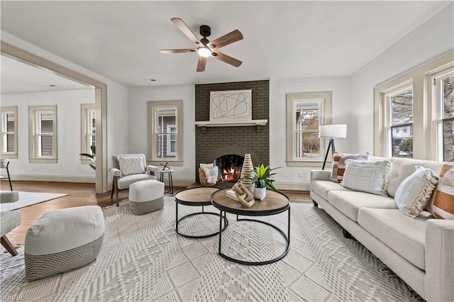 living room with a ceiling fan, a brick fireplace, wood finished floors, and baseboards