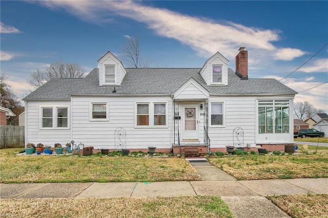 new england style home with a chimney, roof with shingles, a front yard, and fence