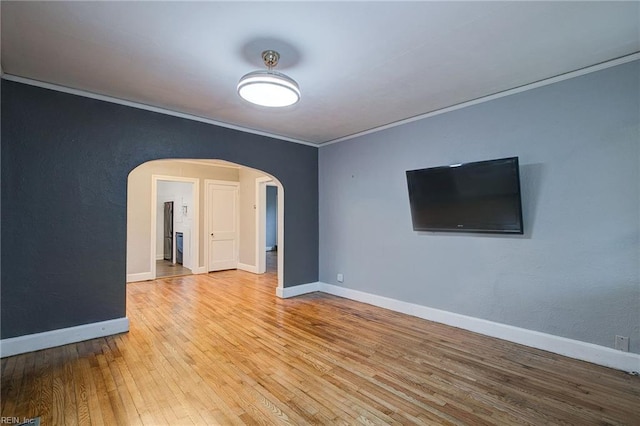 empty room with arched walkways, ornamental molding, baseboards, and wood-type flooring